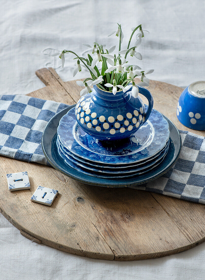 Schneeglöckchen (Galanthus) in blauer Keramikvase auf rustikalem Holzteller