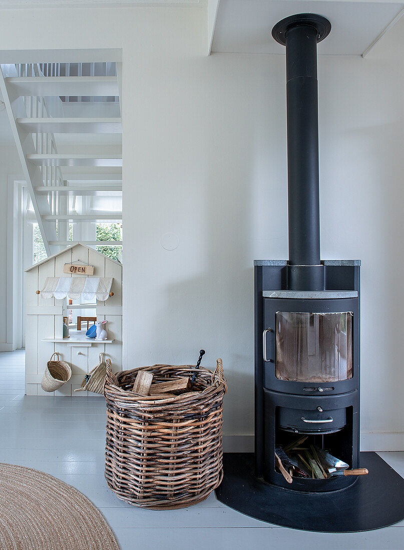 Black wood-burning stove next to wicker basket with logs in bright living room