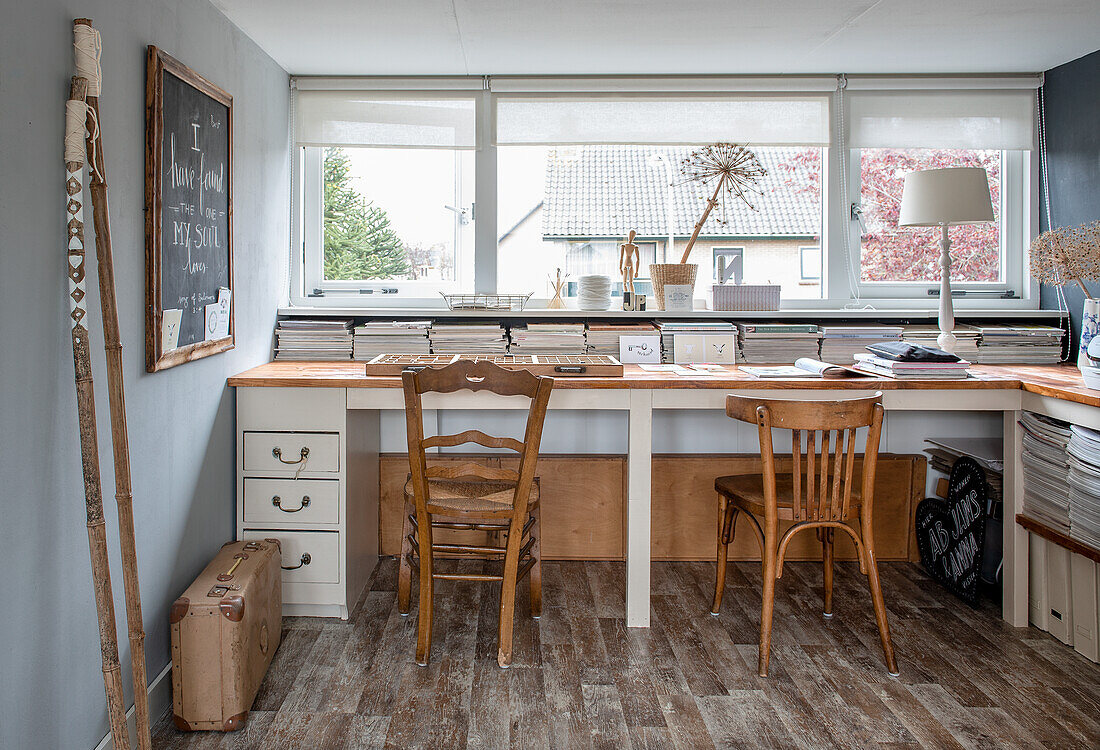 Arbeitszimmer mit zwei Holzstühlen und großem Schreibtisch unter Fensterfront