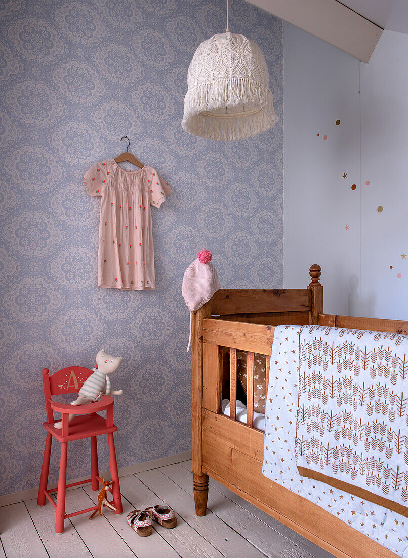 Children's room with patterned wallpaper in lace design, wooden crib and red chair