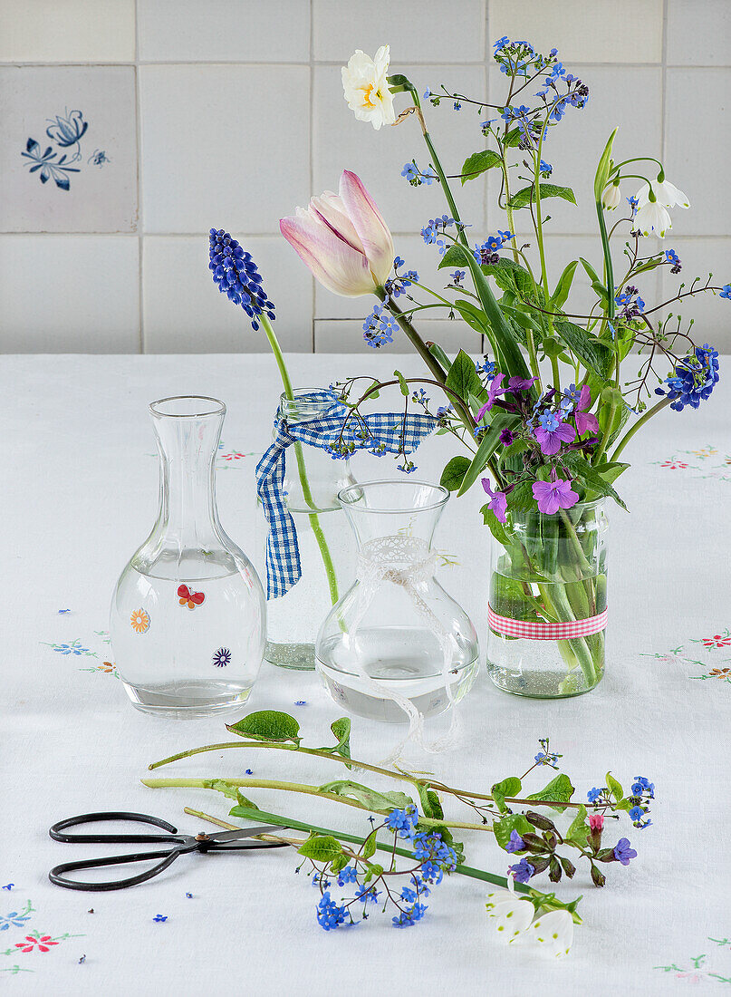 Blumenarrangement aus Tulpen, Vergissmeinnicht und Traubenhyazinthen in Vasen auf weißer Tischdecke