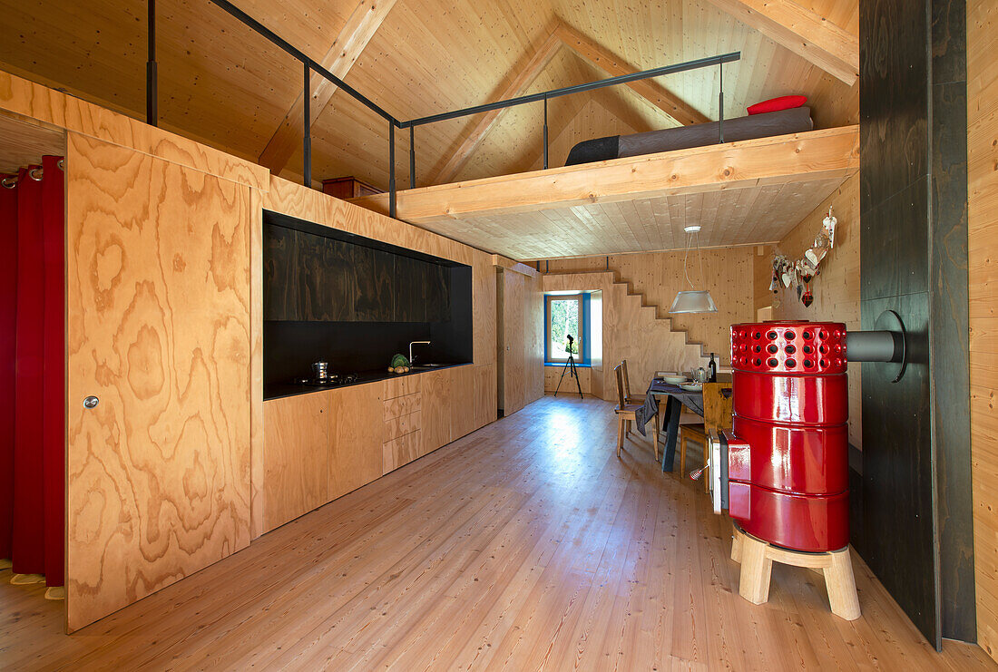 Modern kitchen with wood panelling, red wood-burning stove and open gallery