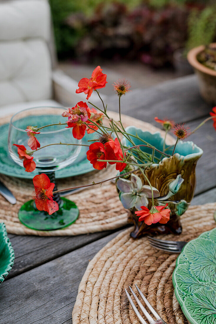 Bouquet of red flowers in a ceramic vase on a rustic wooden table in the garden