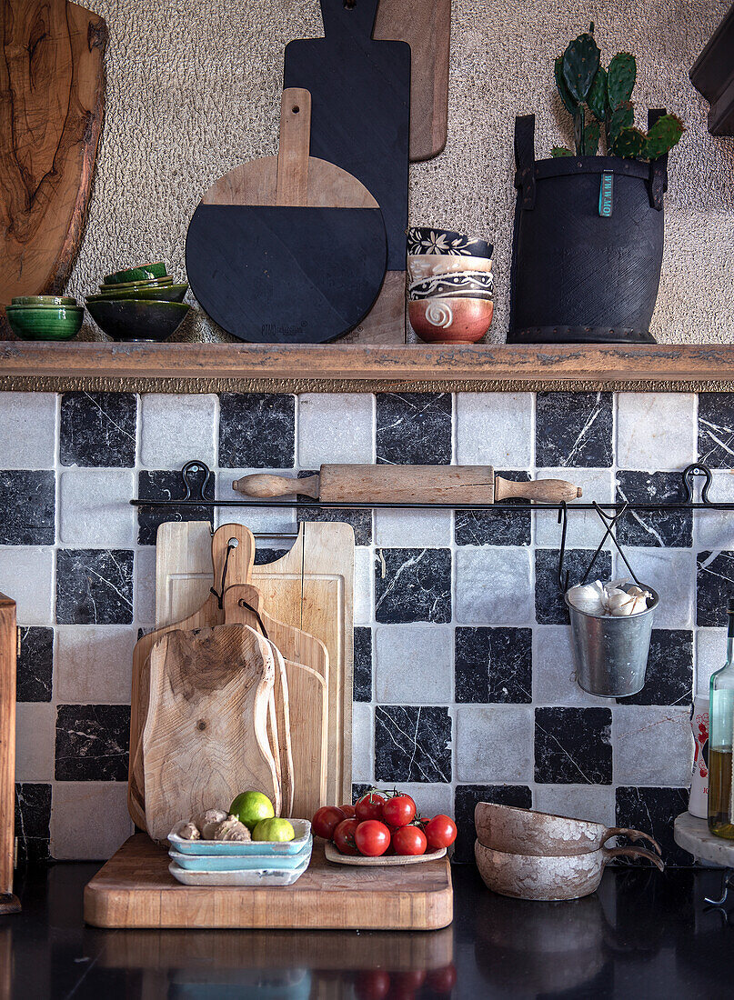 Chopping boards and kitchen utensils in front of a black and white tiled wall in a rustic kitchen