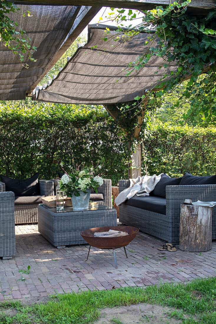 Cozy seating area in the garden with rattan furniture, sunshade and fire pit