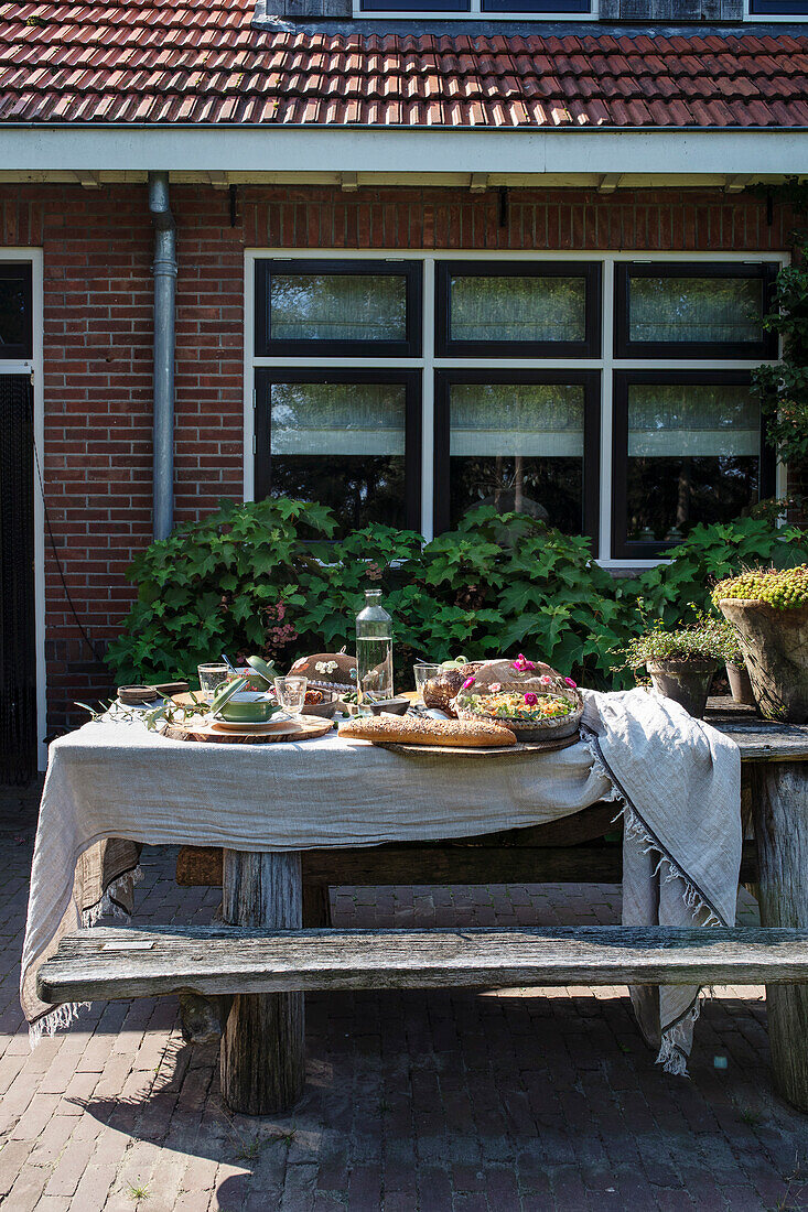 Rustikaler Holztisch mit Sommerbuffet vor Backsteinhaus im Garten