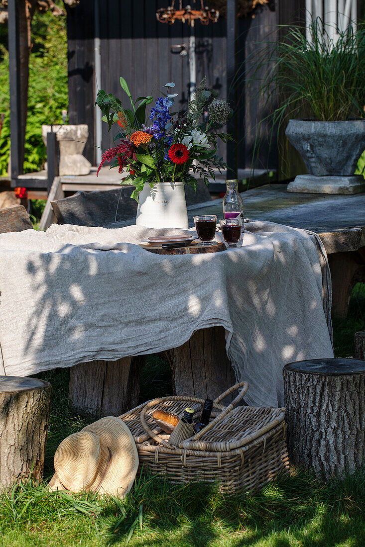 Rustikaler Gartentisch mit Leinentischdecke und Blumenvase, umgeben von Baumstumpfhockern