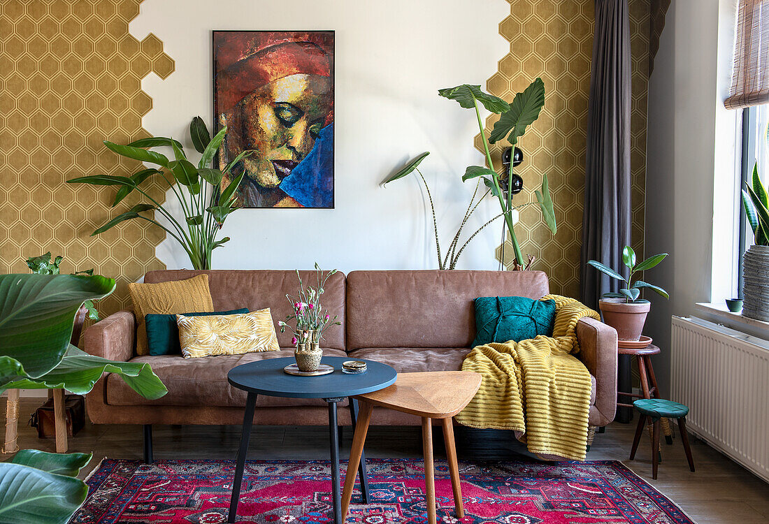 Living room with leather sofa, plants and colourful carpet in front of patterned wallpaper