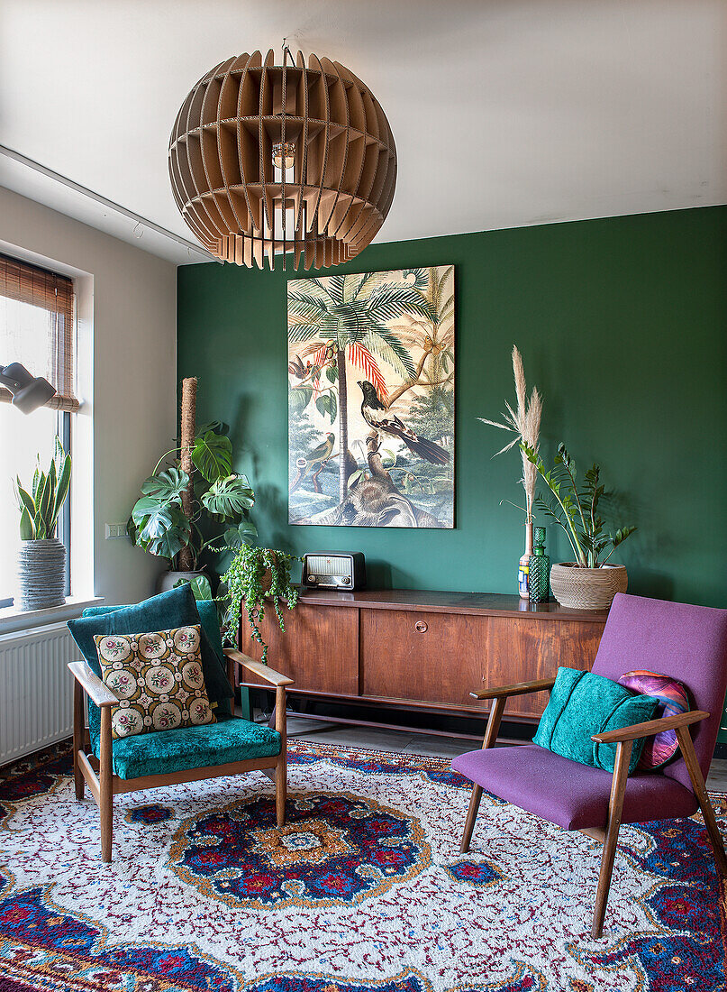 Living room with green accent wall, vintage sideboard and retro armchairs