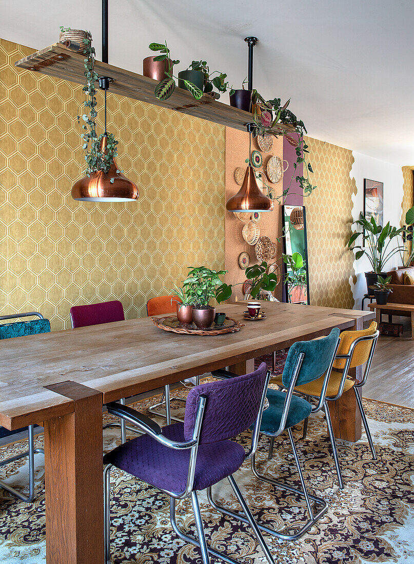 Dining table with colourful chairs and copper lamps in front of golden wallpaper