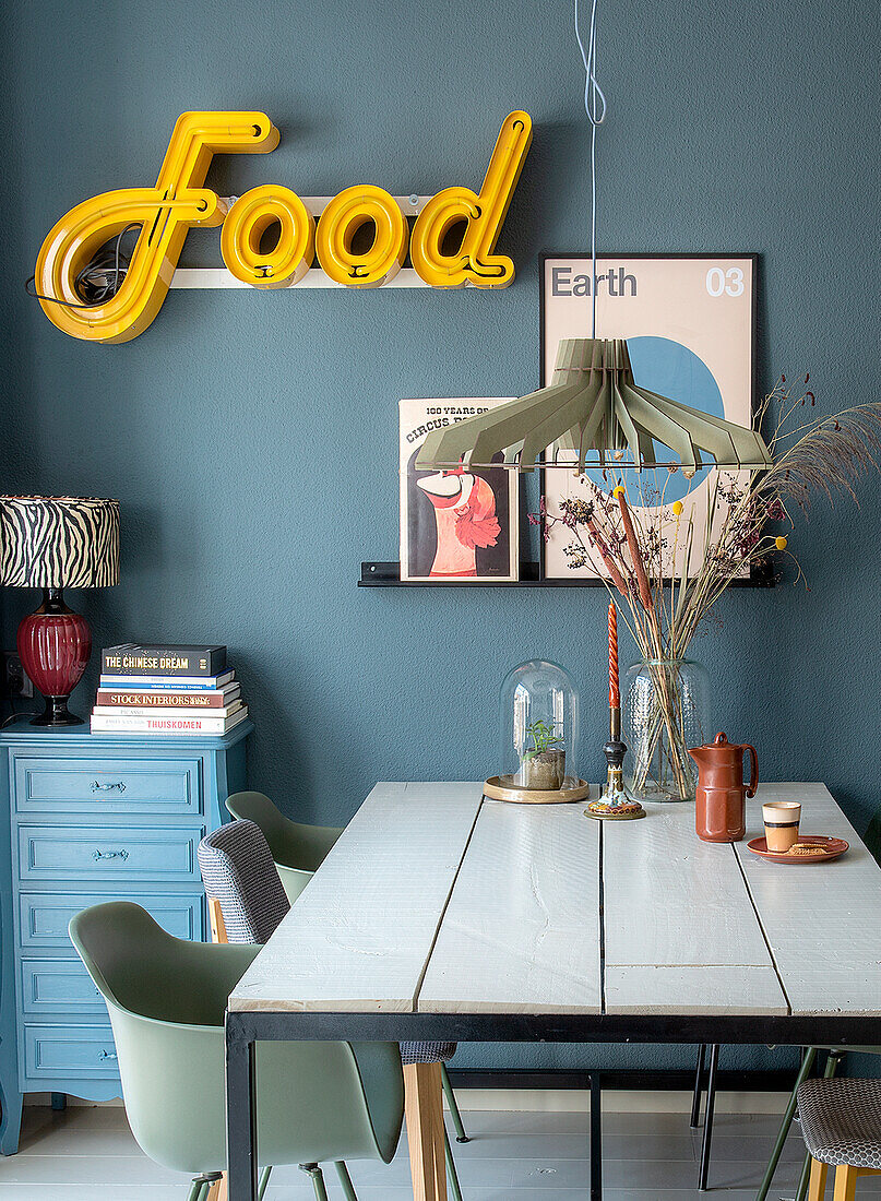 Dining area with blue wall, retro illuminated lettering and decorative posters