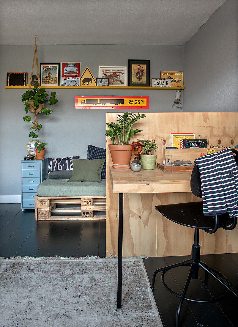 Work area made of light-coloured wood, sofa made of pallets in the background