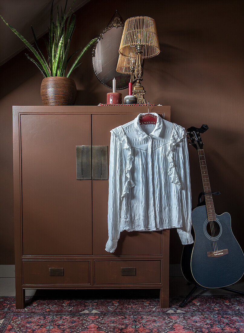 Brauner Schrank mit Retro-Tischlampe, weißer Bluse und Gitarre