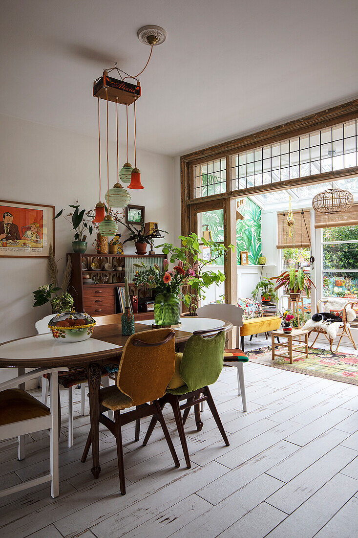 Dining room with retro green and yellow chairs, wooden chest of drawers and lots of plants