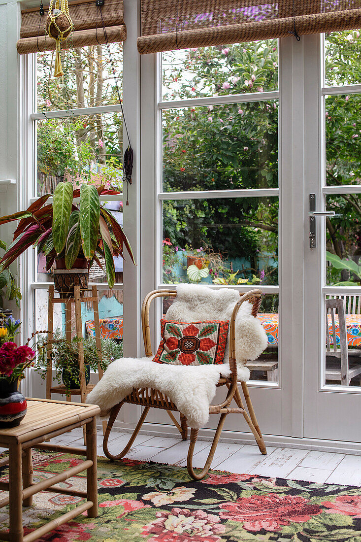 Rattan chair with embroidered cushion and sheepskin in the conservatory