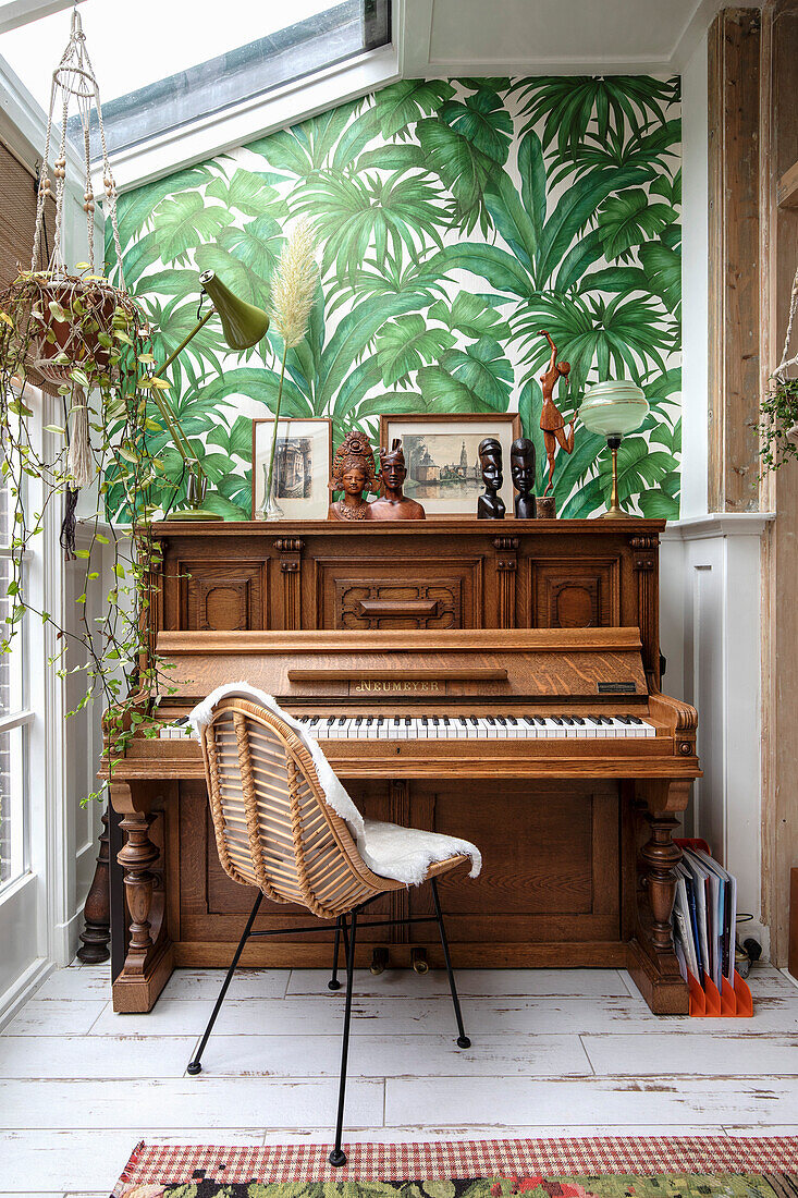 Wooden piano and rattan armchair in front of tropical wallpaper