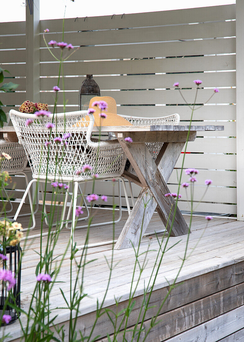 Wooden table and woven chairs on modern patio with white wooden wall