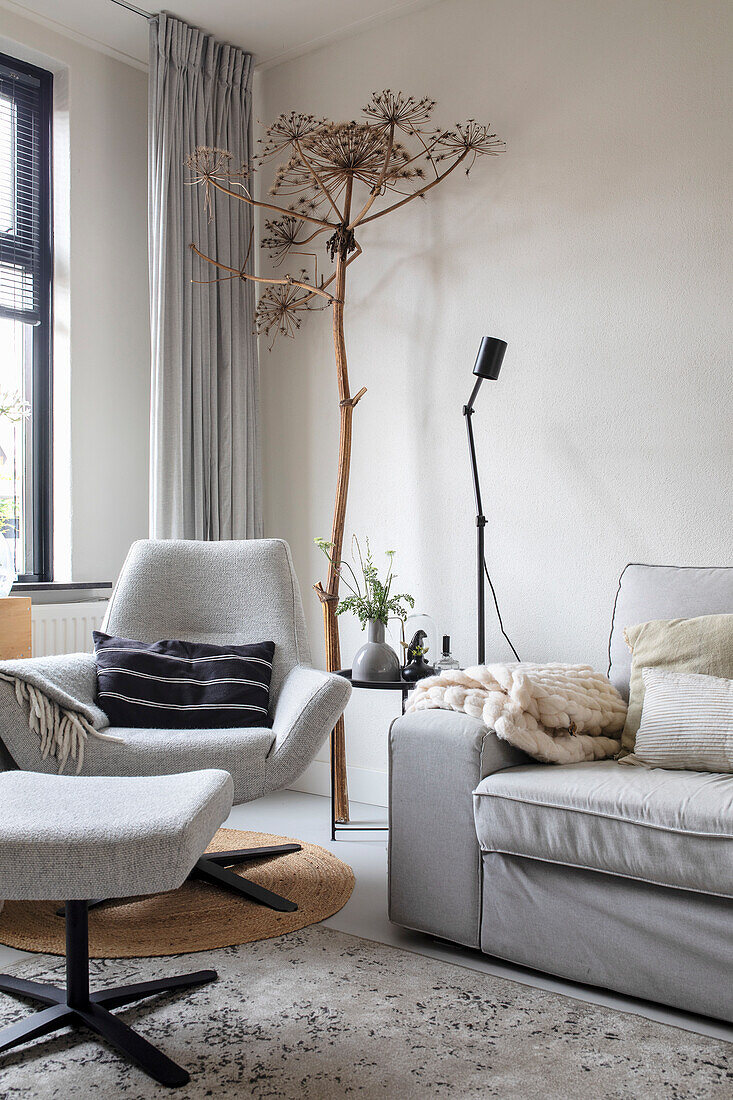 Cosy sitting area with light grey armchair, sofa and dried flower decoration