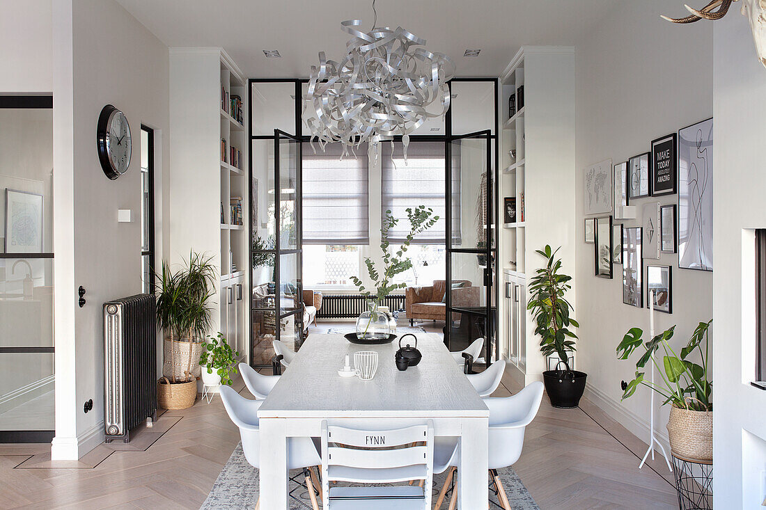 Dining room with white wooden table and modern chairs in front of glazed door with view into living room