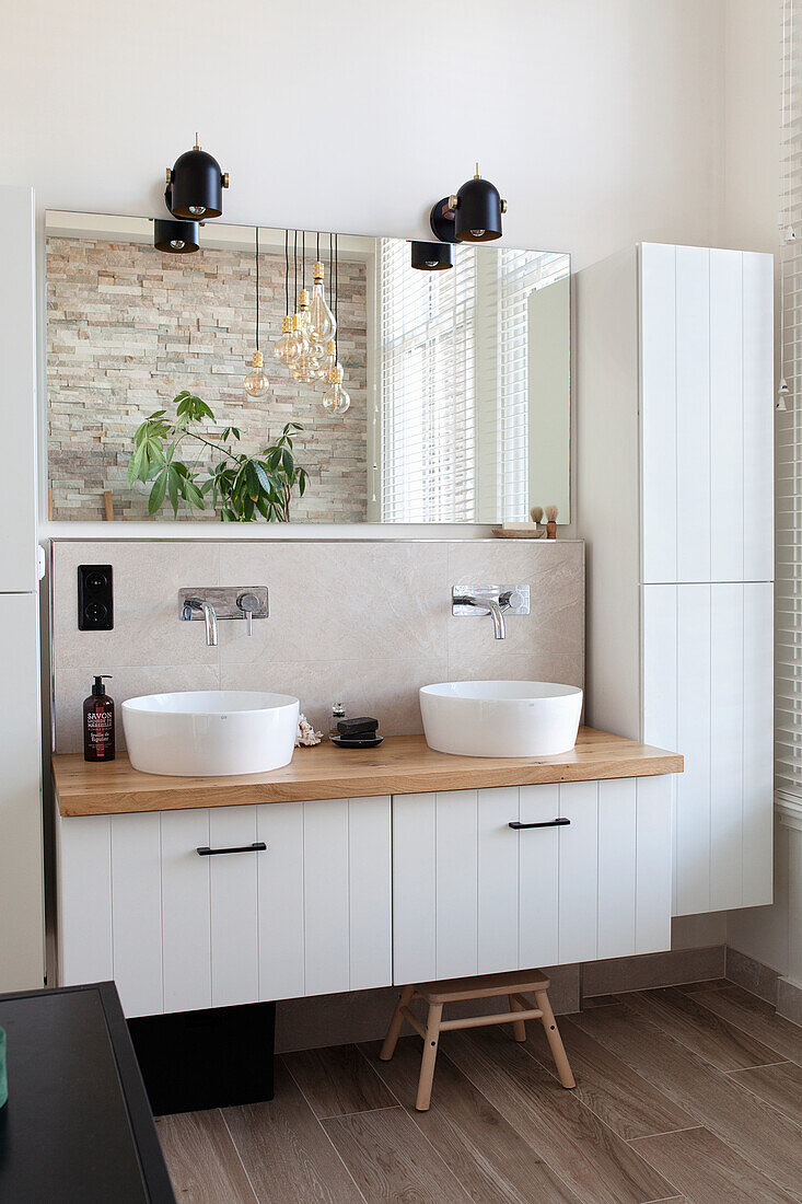 Modern bathroom with double washbasin on wooden countertop and white cabinets