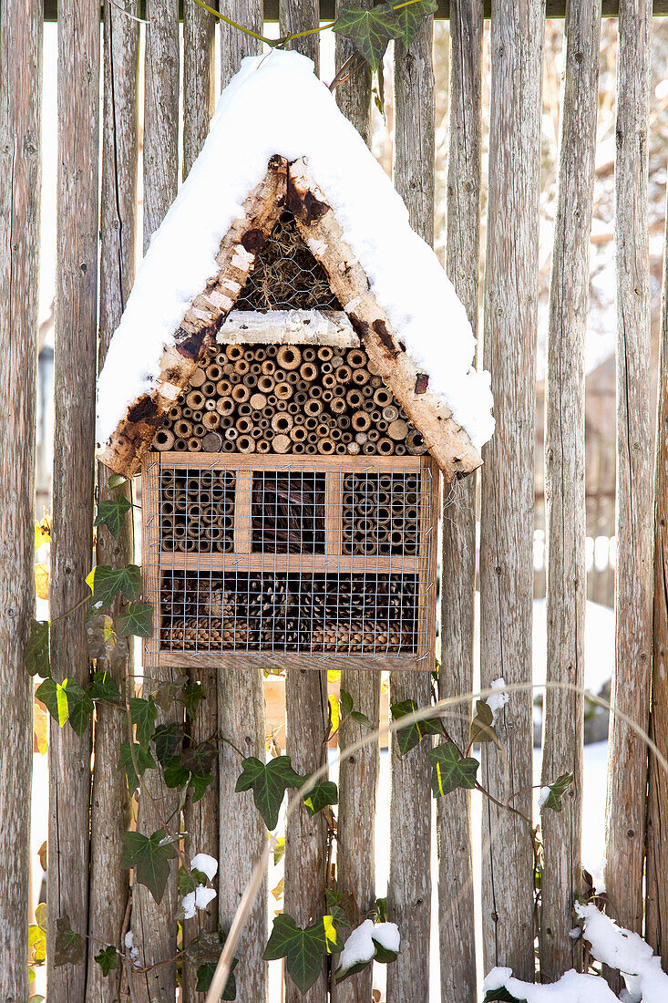 Snow-covered insect hotel made of wood on garden fence