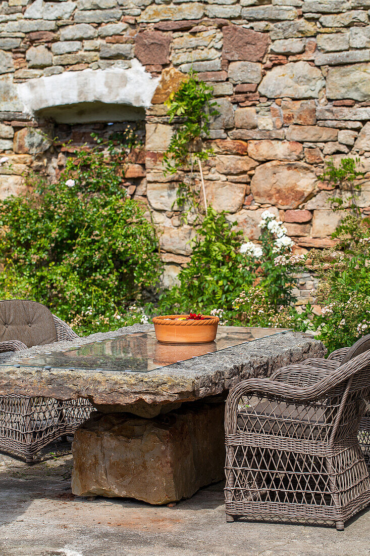 Natural stone table with wicker chairs in front of a brick wall in the garden