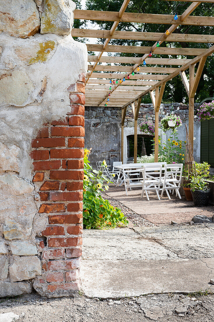 Pergola mit bunter Lichterkette und weißen Gartenmöbeln im Hinterhof