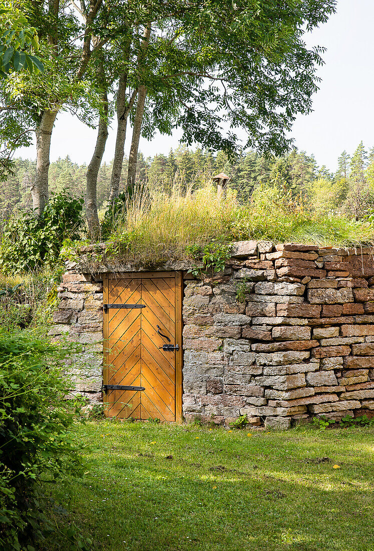 Natursteinmauer mit Holztür und Grasdach im Garten