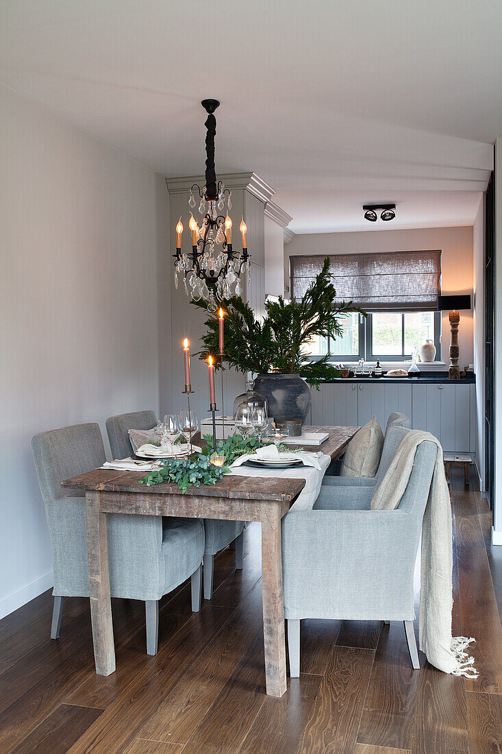 Set wooden dining table with fabric chairs and chandelier with kitchen in the background