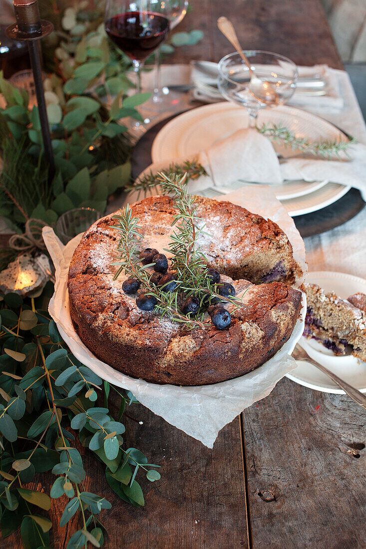 Home-baked blueberry cake with rosemary and icing sugar on a rustic wooden table