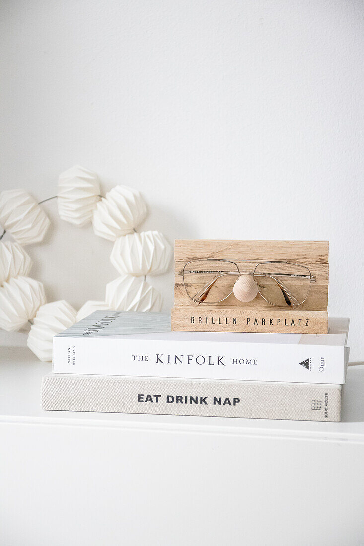 Wooden spectacle holder on a stack of books next to paper lanterns