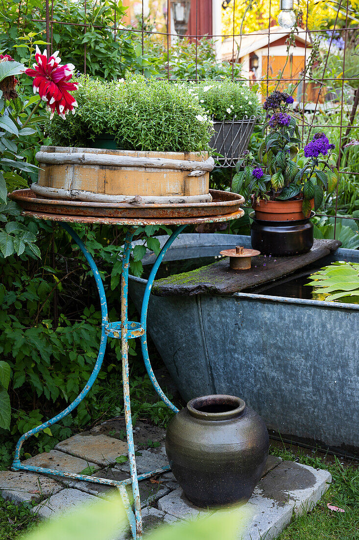 Decorated garden area with round table and potted plants next to zinc tub