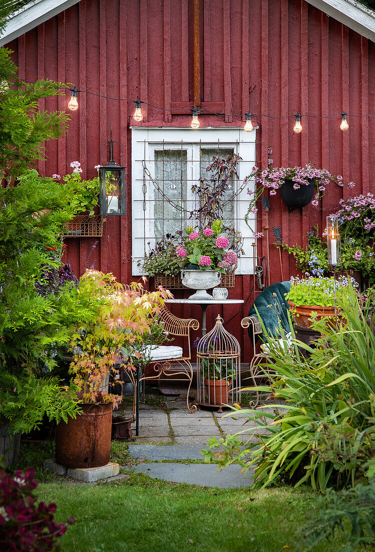 Romantic garden corner with seating area in front of red wooden wall