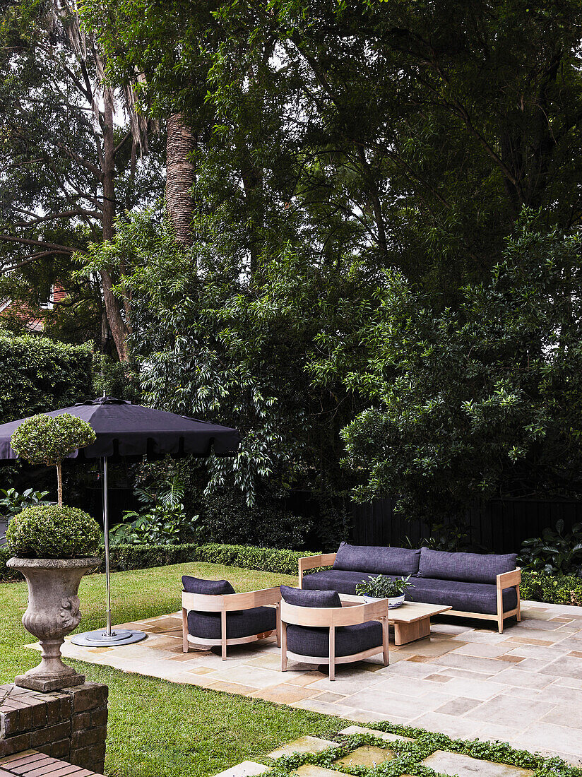 Modern garden lounge area with wooden seating furniture, dark upholstery and parasol