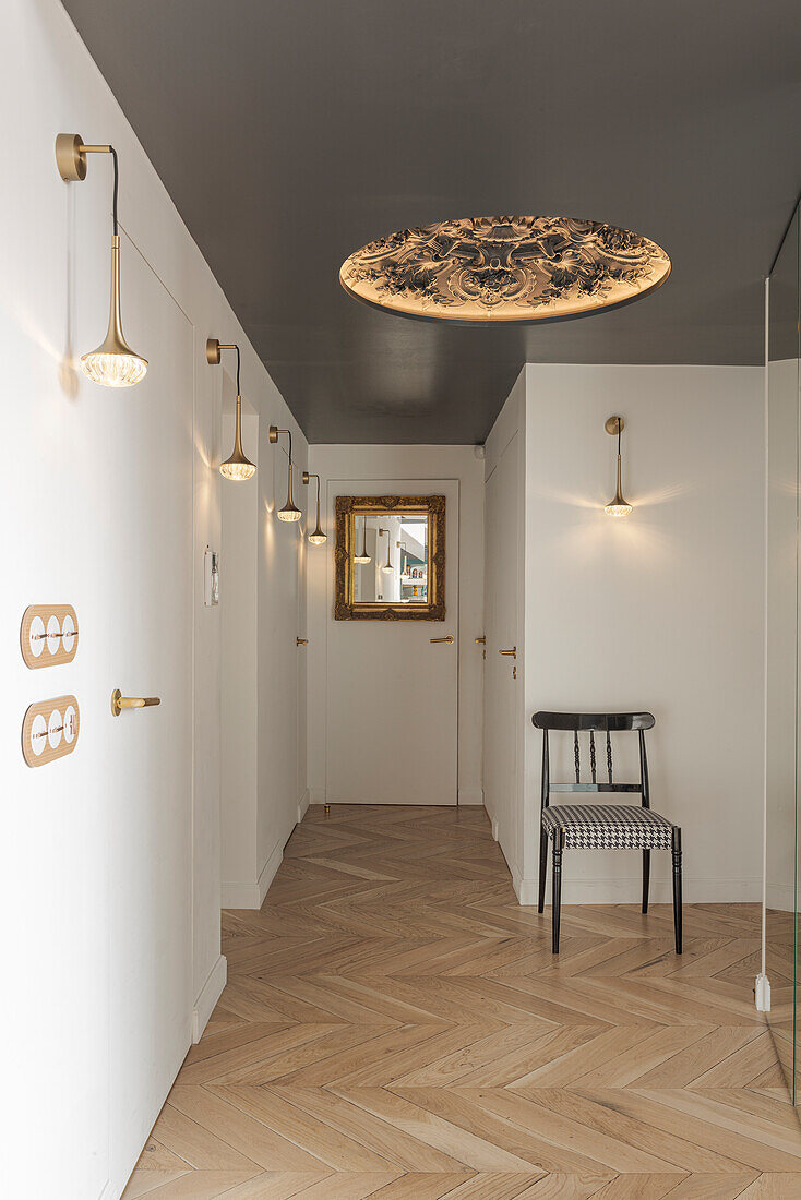 Hallway with herringbone parquet flooring, wall lamps and ornate ceiling chandelier