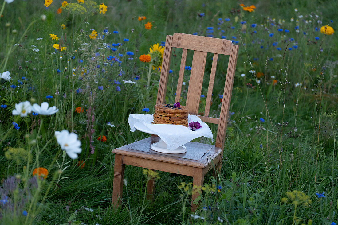 Holzstuhl mit Waffeln auf Tortenplatte in blühender Wiese