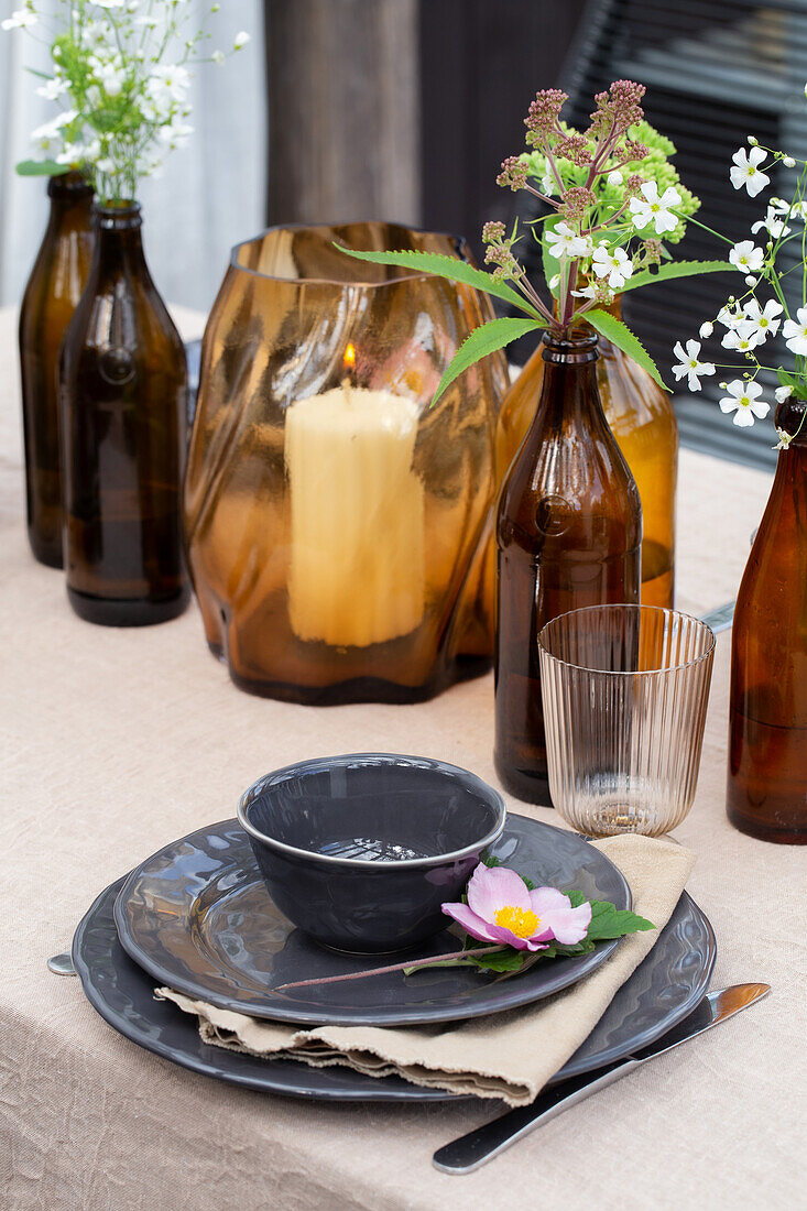 Gedeckter Tisch mit Keramikgeschirr, braunen Glasflaschen und Kerzenlicht