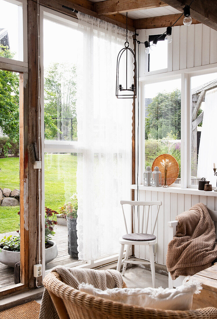 Lichtdurchfluteter Raum mit Korbsessel, weißem Stuhl und Gartenblick