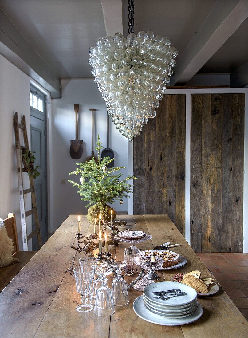 Rustic dining table with candles and Christmas decorations under a large glass lamp