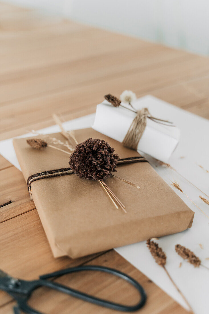 Verpackte Geschenke mit Naturmaterialien und Pompons auf Holztisch