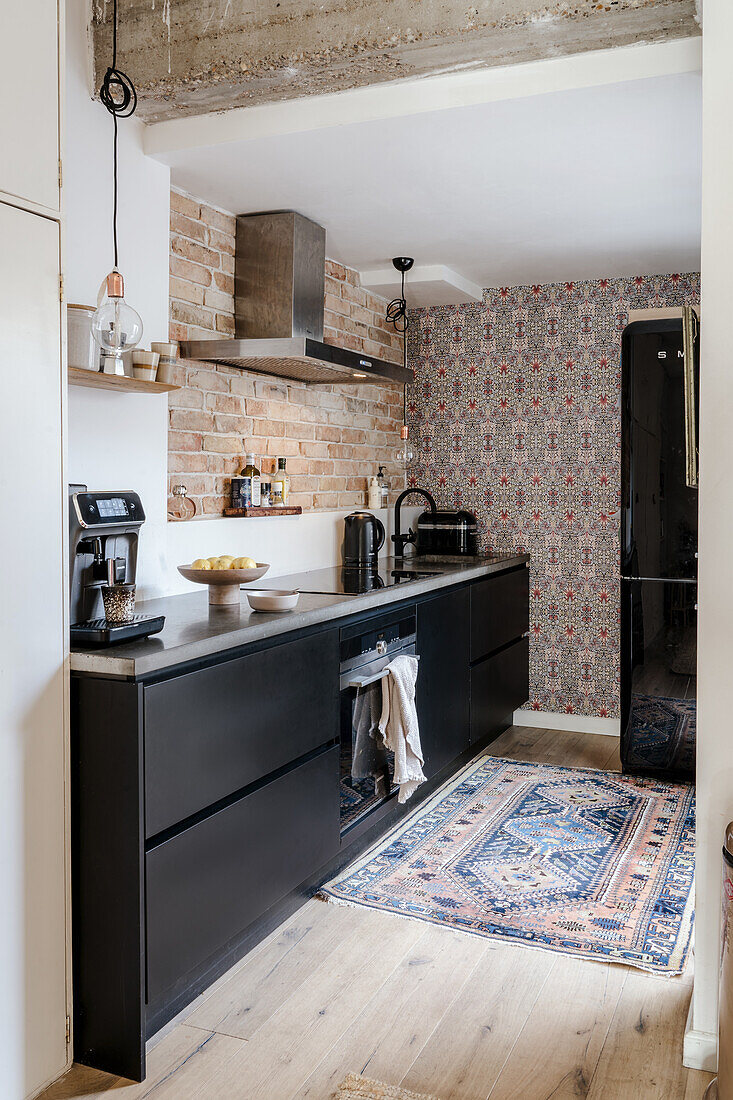 Black kitchen cupboards with brick wall, patterned wallpaper and oriental carpet