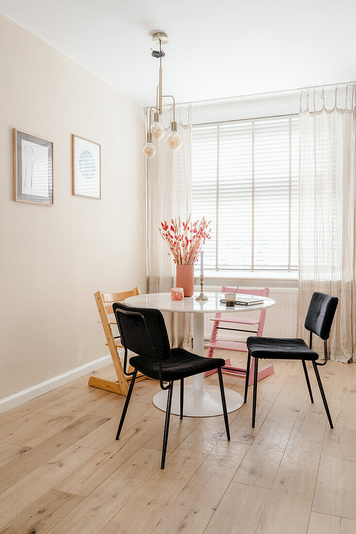 Round dining table with modern black chairs in front of window with translucent curtains