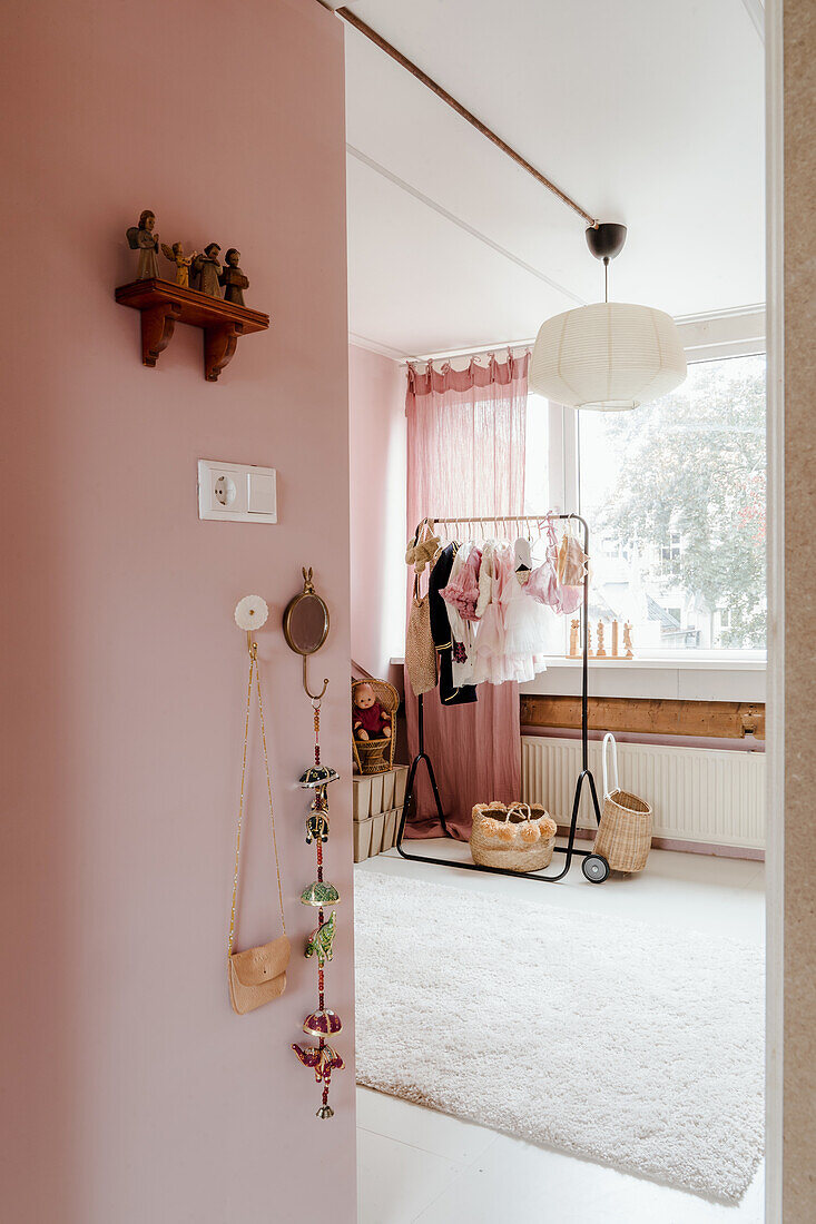 Children's room with pink walls and clothes rack next to window