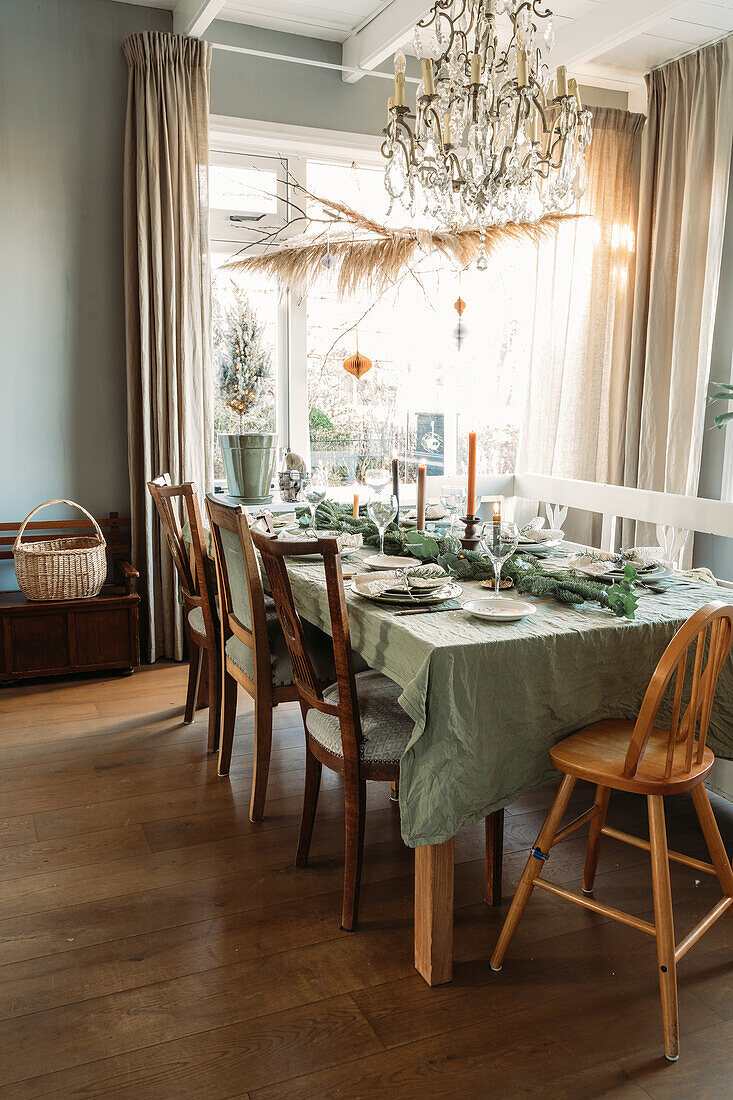 Dining table set with a green tablecloth and wooden furniture under a chandelier