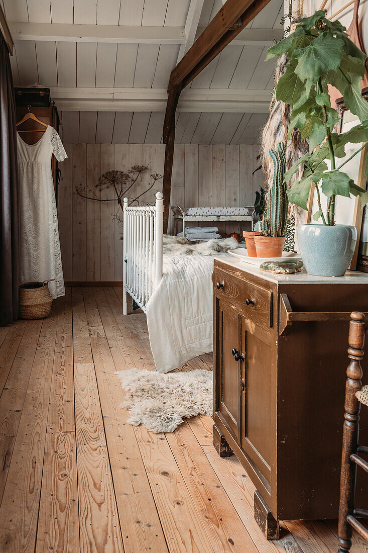 Rustic bedroom with wooden floor, plants and antique chest of drawers