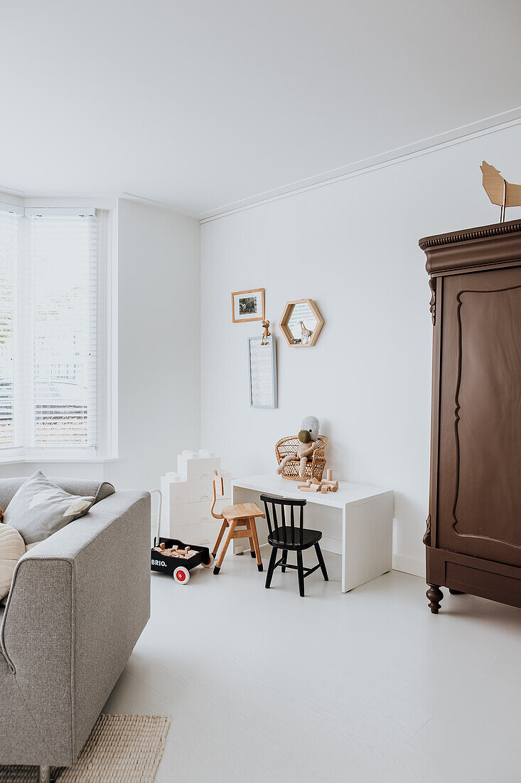 Kinderecke mit Spielzeug, kleinem Tisch und Stühlen in Wohnzimmer mit weißer Wand und Holzschrank