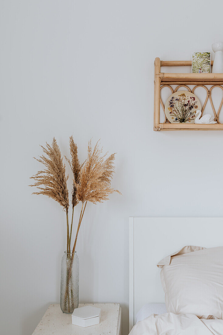 Schlafzimmer mit Trockenblumen in Glasvase und Wandregal aus Rattan