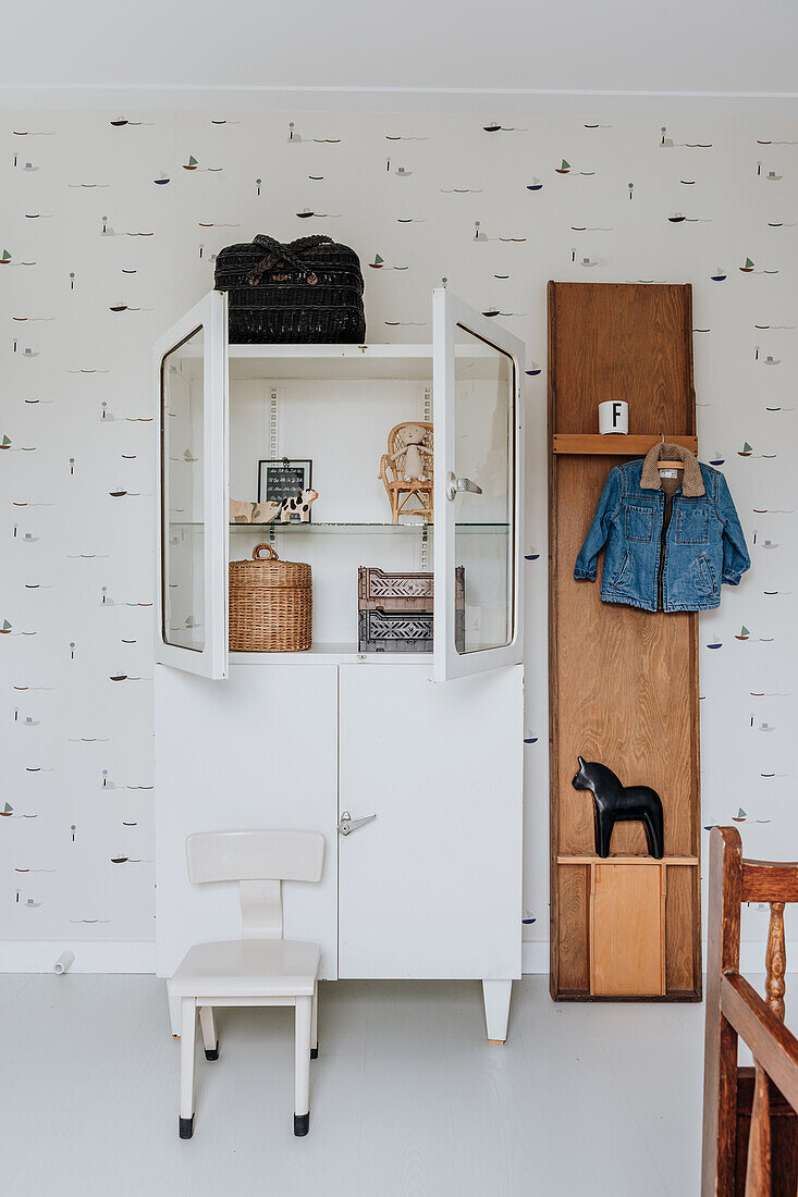 White wardrobe with open glass doors and high chair in the children's room