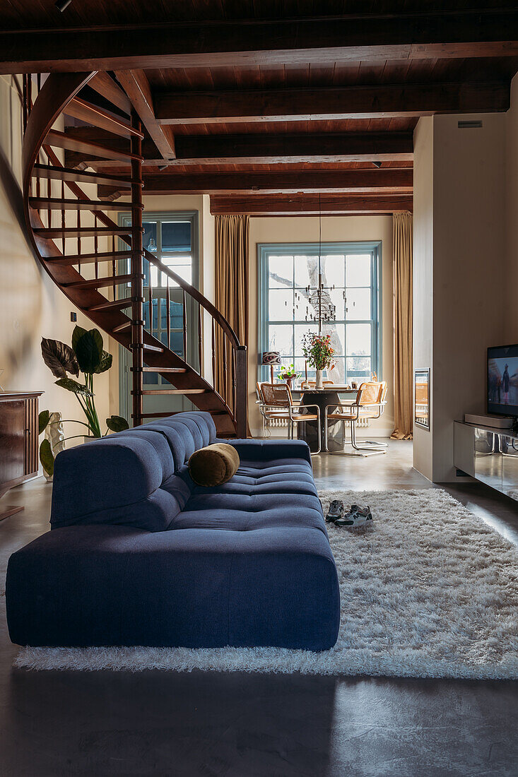 Open-plan living area with blue sofa landscape and wooden spiral staircase