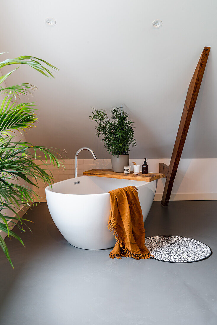 Freestanding bathtub in modern bathroom with wooden accents and plants